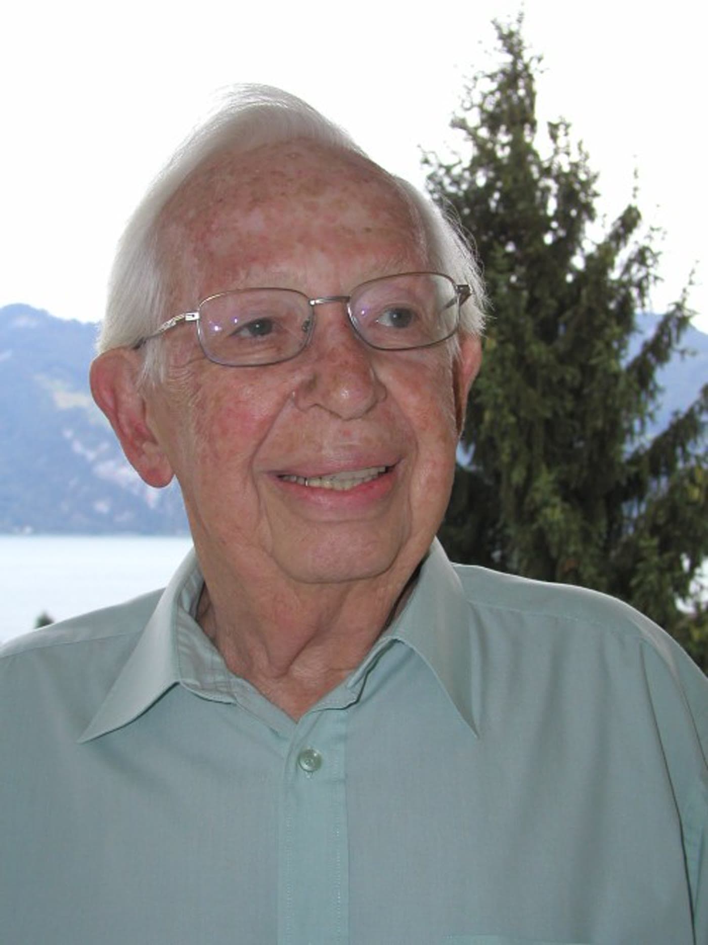 Frank Alper im Freien, hinter ihm ein See und Berge.