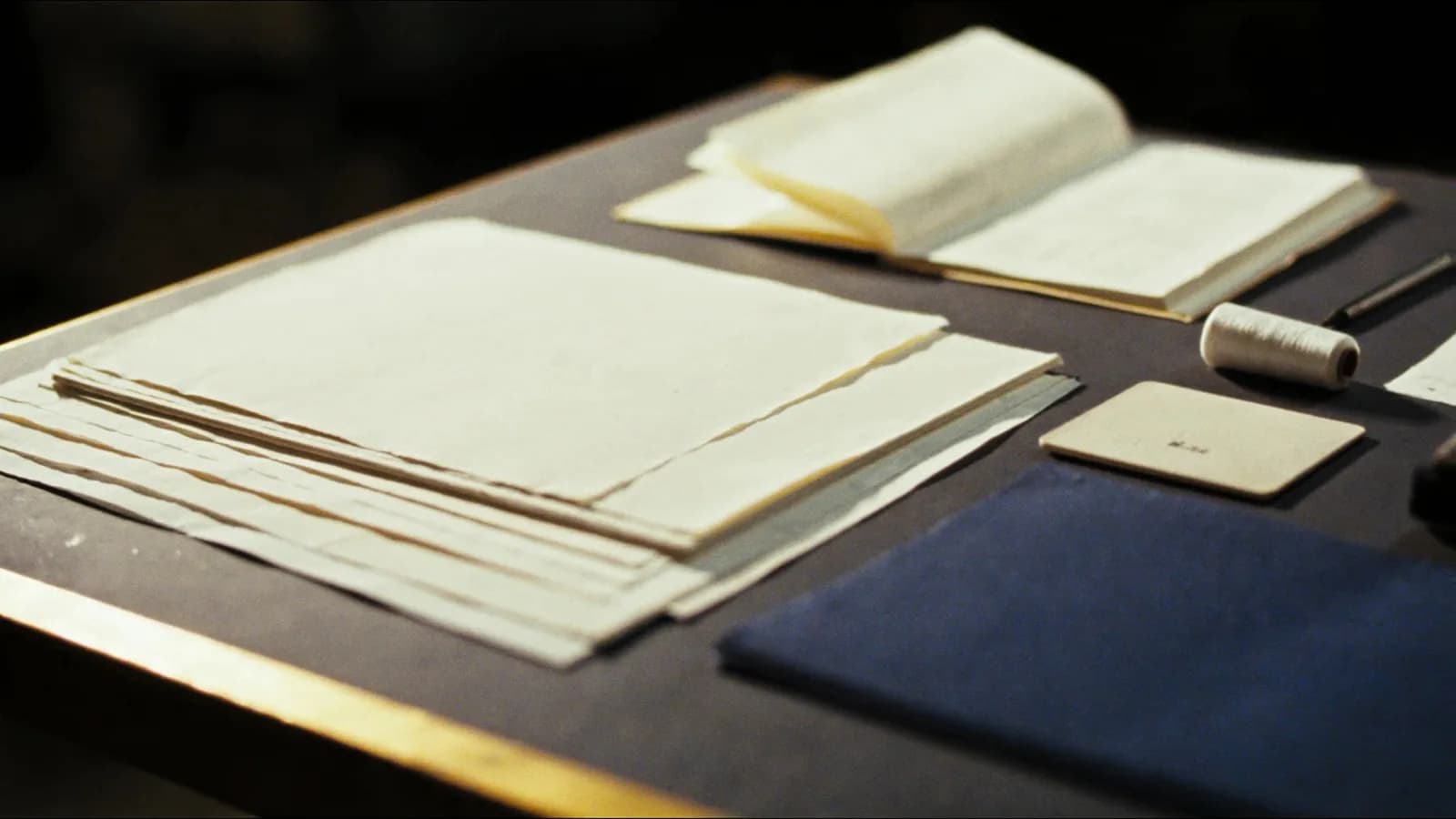 Illustration: ein Arbeitstisch des Verlags mit Büttenpapier, gefalzten Bogen und Buchleinen, durchzogen von einem goldenen Faden.
