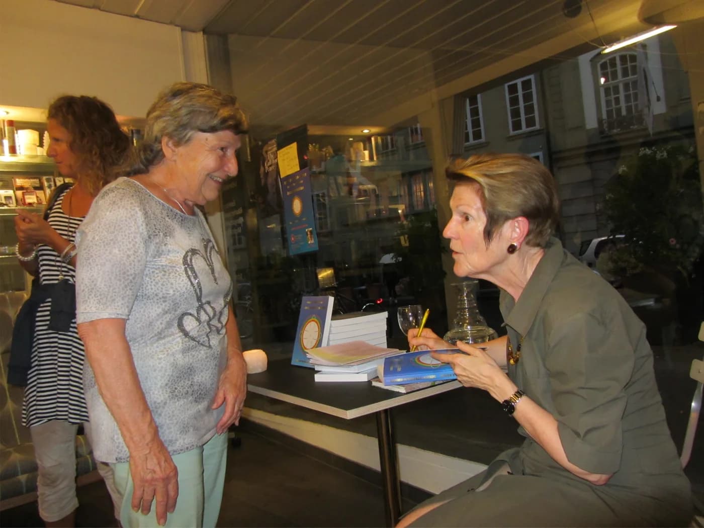 Ursula M. Frick Albrecht signiert an einem Tisch ein Exemplar von „Seelen-Strahlen-Kinder“ und spricht mit einer Leserin.